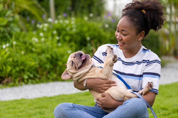 Jovem mulher sentada na grama segurando seu Bulldog Francês